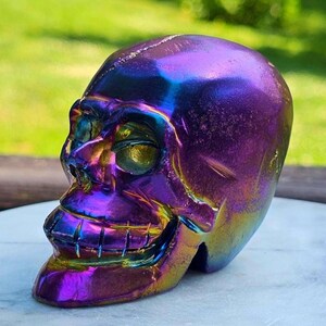 May include: A decorative skull sculpture with an iridescent finish. The skull is a blend of purple, blue, and gold, creating a shimmering effect. A unique decorative item.