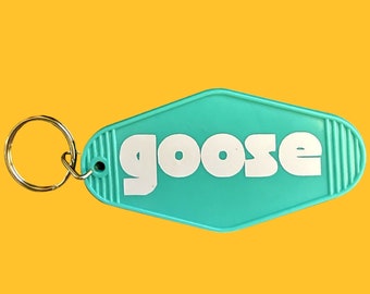 May include: A turquoise blue key chain with a white "goose" logo in a retro motel key shape.