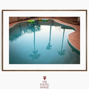 Puede incluir: Una piscina azul con el reflejo de palmeras en el agua. Hay dos flotadores inflables flotando en la piscina.