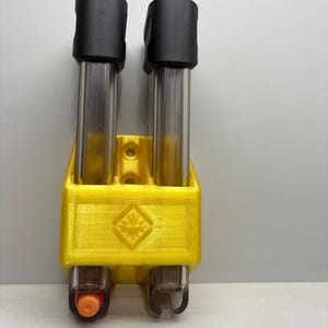 May include: A yellow 3D printed magazine holder with two black magazine holders and a silver magazine inside each. The magazine holder has a diamond shape with a snowflake design in the centre.