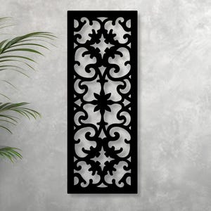 May include: A black, rectangular decorative panel with an intricate, symmetrical cutout design. The pattern features swirling shapes and floral elements, creating a visually appealing, openwork aesthetic. The panel is mounted against a light gray wall.