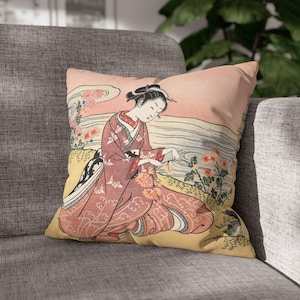 May include: A decorative throw pillow with a vintage Japanese print of a woman in a pink kimono sitting by a body of water with flowers. The background is a light pink with a white cloud.