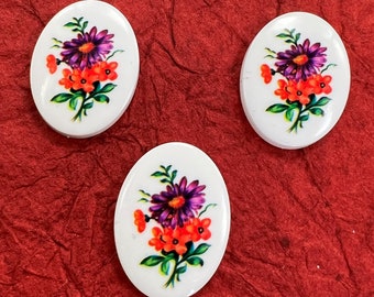 May include: Three white oval-shaped buttons with a floral design. The flowers are purple, orange, and green.