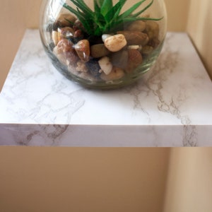 May include: A white marble shelf with a clear glass vase filled with small stones and a green succulent plant.