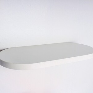 May include: White oval-shaped floating shelf mounted on a white wall.