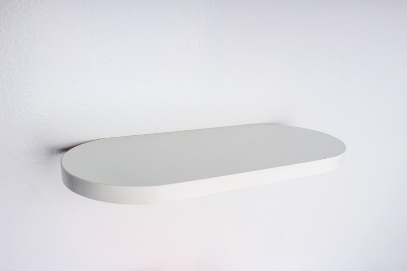 May include: White oval-shaped floating shelf mounted on a white wall.