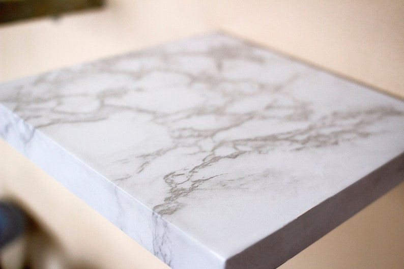 May include: A white shelf with a marble-like pattern. The shelf is made of a smooth, white material and has a slightly raised edge.