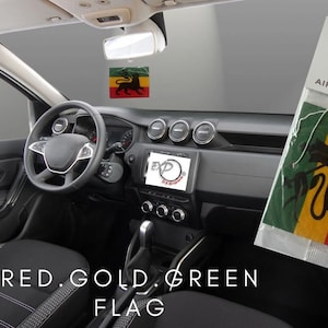Puede incluir: Un ambientador de coche rojo, dorado y verde con un gráfico de león. El ambientador está colgado del espejo retrovisor de un coche. El texto "EXP Designs Air Fresheners" está impreso en el embalaje. El texto "RED. GOLD. GREEN FLAG" está impreso debajo del ambientador.