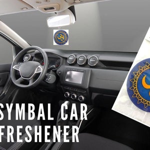 May include: A car air freshener with an Aum symbol in a blue and gold design. The air freshener is hanging from the rearview mirror of a car. The packaging reads "EXP Designs Air Fresheners".