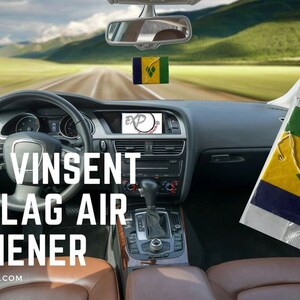 May include: A car air freshener featuring the Saint Vincent and the Grenadines flag. The flag is green, yellow, and blue with a white border. The air freshener is hanging from the rearview mirror of a car driving down a road.