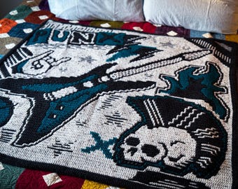 Può includere: Una coperta all'uncinetto a tema punk rock. Presenta un teschio, una chitarra e la parola "Punk" in filato bianco e nero su uno sfondo bianco.