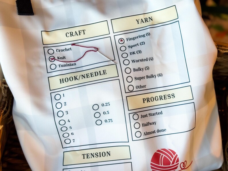 Pode incluir: Saco de tecido branco para projetos de tric&ocirc; com uma lista de verifica&ccedil;&atilde;o para trabalhos de agulha. A lista de verifica&ccedil;&atilde;o inclui se&ccedil;&otilde;es para o tipo de trabalho, o tamanho da agulha/croch&ecirc;, o peso do fio, a tens&atilde;o e o progresso. A bolsa tem um gr&aacute;fico de novelo de l&atilde; vermelho.