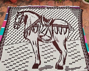 May include: A large, rectangular blanket featuring a detailed image of a horse in brown against a white background. The horse is saddled and bridled. The blanket has a decorative border and a repeating pattern.