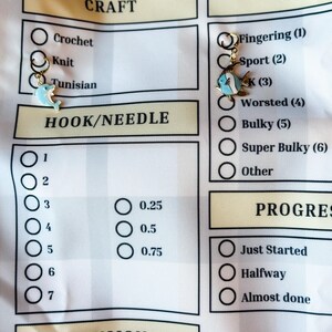 Pode incluir: Uma lista de verifica&ccedil;&atilde;o branca com um cabe&ccedil;alho amarelo para projetos de artesanato. A lista de verifica&ccedil;&atilde;o inclui se&ccedil;&otilde;es para artesanato, fio, gancho/agulha, tens&atilde;o e progresso. A lista de verifica&ccedil;&atilde;o tem um amuleto de golfinho e um amuleto de peixe.