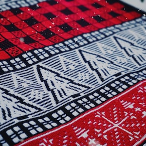Può includere: Un maglione di lana rosso e bianco con un motivo di alberi di Natale e fiocchi di neve. Il maglione è realizzato in un materiale morbido e caldo ed è perfetto per le festività natalizie.