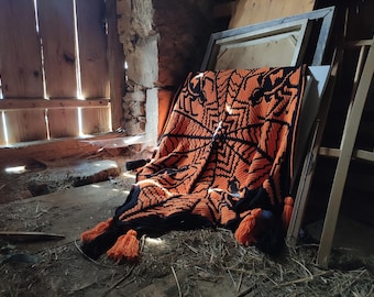May include: A crocheted throw blanket with a geometric pattern in orange and black. The blanket is lying on a wooden floor in a rustic setting.
