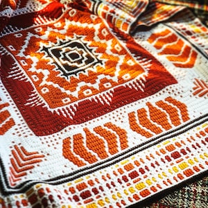 以下が含まれることがあります： オレンジ、赤、白の幾何学模様のクロシェ編み毛布
