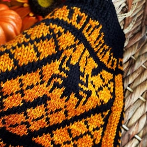 May include: Black and orange knitted sock with a spider web pattern. The sock is partially tucked into a wicker basket.