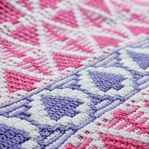 May include: Close-up of a crocheted fabric with a geometric pattern in pink, white, and purple.