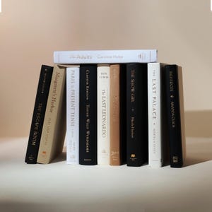 May include: A collection of hardcover books with various titles and authors, including "The Adults" by Caroline Hulse and "The Escape Room" by Megan Goldin. The books are in various colors, including black, white, and tan.