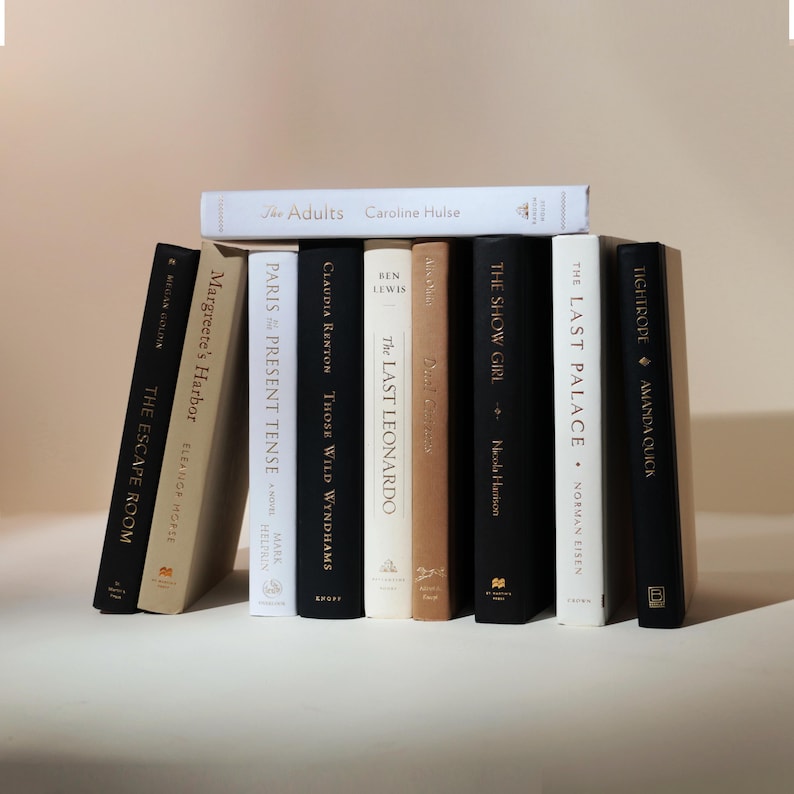 May include: A collection of hardcover books with various titles and authors, including "The Adults" by Caroline Hulse and "The Escape Room" by Megan Goldin. The books are in various colors, including black, white, and tan.