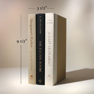 May include: Three hardcover books, 9 1/2 inches tall and 3 1/2 inches wide, with titles including "Margreete's Harbor," "The Escape Room," and "The Last Leonardo." The books have varying colors, including beige, black, and white.