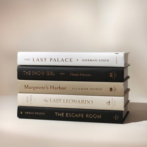 May include: A stack of five hardcover books with various titles and authors. The books have covers in white, black, and beige, with gold lettering. Titles include "The Last Palace," "The Show Girl," and "The Escape Room."