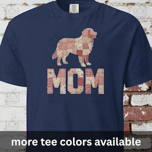 May include: Navy blue t-shirt featuring a patchwork-style dog graphic above the word "MOM" in a similar patchwork design. The shirt has short sleeves and a crew neck. The text "more tee colors available" is at the bottom.