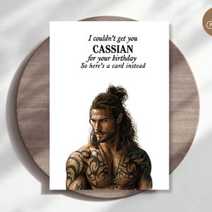 May include: A white greeting card featuring a muscular man with long brown hair in a top knot and extensive black tribal tattoos on his chest and shoulders. The text reads: I couldn't get you CASSIAN for your birthday. So here's a card instead.