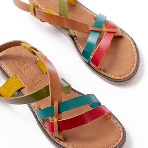 May include: Leather sandals with a multi-colored strap design. The sandals feature straps in yellow, green, red, and teal. The footbed is a light brown color with a stitched border. The sandals have a buckle closure and the text "INFONE" is visible.