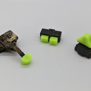 Puede incluir: Tres tipos diferentes de interruptores eléctricos con botones de plástico verde. Los interruptores son negros y tienen una variedad de formas y tamaños.