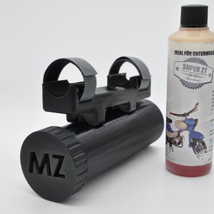 May include: A black plastic tube with a black cap that says "MZ" on it. The tube is attached to a black metal bracket with two gray straps. The tube is next to a clear bottle with red liquid and a white label that says "IDEAL FUR UNTERWEGS SUPER 2T MZ 400 2-Takt-Benzinöl".