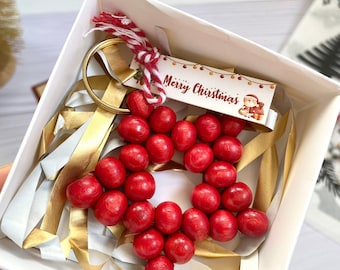 May include: A red wooden star-shaped keychain with a gold ring and a white tag that says "Merry Christmas" with a cartoon Santa Claus illustration.