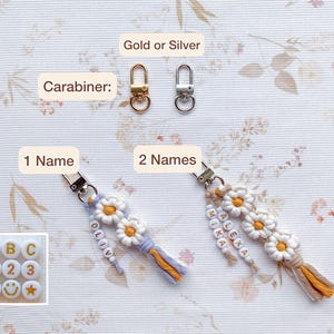 May include: Two keychains with daisy-shaped charms and colorful beads. The keychain on the left has the name "Olivia" spelled out in beads and the keychain on the right has the names "Alexa" and "Mika" spelled out in beads. Both keychains have a gold or silver carabiner.