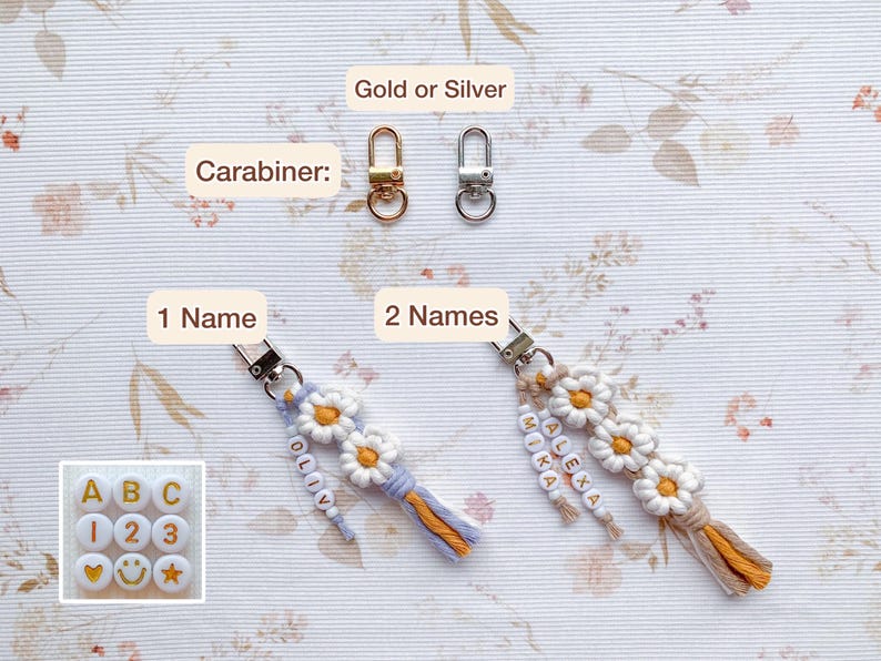 May include: Two keychains with daisy-shaped charms and colorful beads. The keychain on the left has the name "Olivia" spelled out in beads and the keychain on the right has the names "Alexa" and "Mika" spelled out in beads. Both keychains have a gold or silver carabiner.