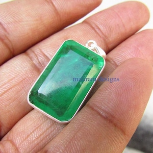 May include: A rectangular pendant featuring a large, vivid green gemstone set within a silver-coloured metal frame. The gemstone has a faceted surface, and the pendant has a small loop at the top for a chain. The text "marram designs" is visible.