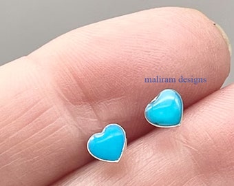 Puede incluir: Un par de pendientes de botón en forma de corazón. Cada pendiente presenta un centro turquesa brillante con un borde plateado. El texto "maliram designs" es visible en el fondo.