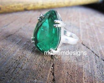 May include: A sterling silver ring featuring a large, pear-shaped, emerald-green gemstone. The ring has a unique design with small decorative accents around the stone and the text "mairamdesigns" on the surface.