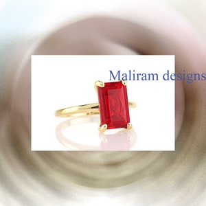 May include: A gold ring featuring a rectangular, vibrant red gemstone. The ring has a slender band and a four-prong setting. The text "Maliram designs" is visible in the image.