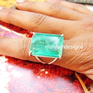May include: A silver ring featuring a large, rectangular, emerald-green gemstone. The ring's band is a simple, thin silver design. The text "maliramdesigns" is visible on the gemstone.