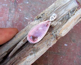 May include: A teardrop-shaped pendant with a pink gemstone set in a silver bezel. The pendant is displayed on a piece of wood. The text "maliramdesigns" is visible on the wood.