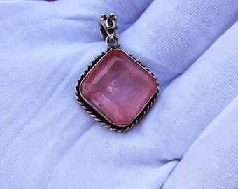 May include: A silver pendant with a large, square, pink gemstone. The gemstone is set in a silver frame with a twisted rope design. The pendant has a small loop at the top for a chain.