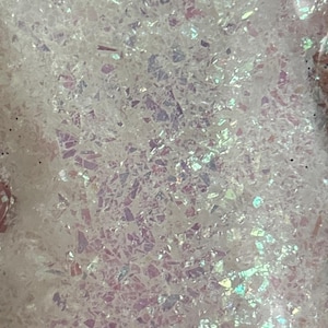 Peut inclure: Gros plan sur des paillettes irisées, sur fond blanc. Les paillettes sont composées de petits morceaux irréguliers de matière irisée.