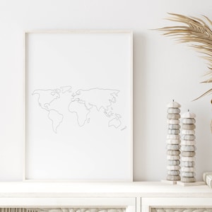 Könnte beinhalten: Ein weißer gerahmter Druck mit einer einfachen Linienzeichnung einer Weltkarte auf weißem Hintergrund. Der Druck befindet sich auf einem weißen Regal mit einer Vase mit getrockneten Palmblättern und zwei Stapeln weißen Dekorationsgegenständen.