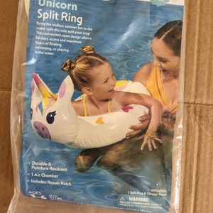 May include: A white unicorn split ring pool float with pink and purple details. The float is 1 foot 5 inches wide and is designed for ages 3-6 and up to 44 lbs. It includes a repair patch. The image shows a child and an adult in a pool using the float.