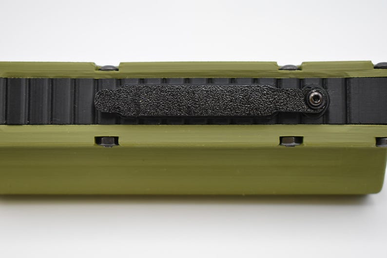 May include: A green and black rectangular case with a black strap and a small screw on the side.