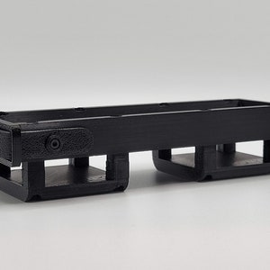 Puede incluir: Caja de almacenamiento de plástico negro impresa en 3D con dos compartimentos. La caja tiene una superficie texturizada y un pequeño agujero en el lateral.