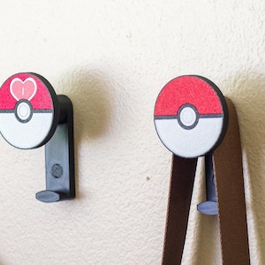 May include: Five black metal wall hooks with colorful, circular designs. Each hook features a different design, including red, yellow, green, and blue accents. A purple bag and brown straps hang from some of the hooks.