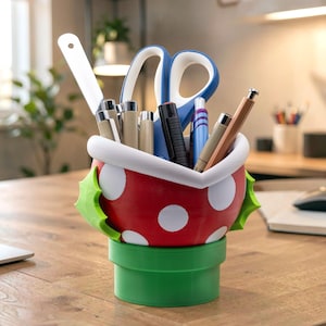 May include: A red and white polka-dot desk organiser shaped like a plant, featuring a green base and two green leaves on the sides. The container holds various office supplies, including a pair of blue and white scissors, pens, and a ruler.