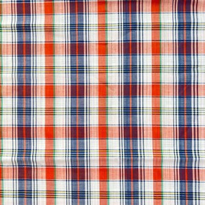 May include: A red, white, and blue plaid fabric with a subtle green stripe. The fabric has a woven texture and is slightly wrinkled.